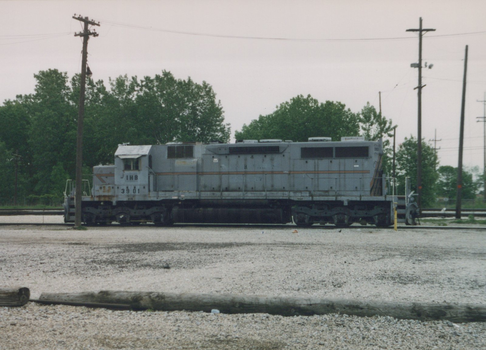 A gray six-axle diesel locomotive lettered IHB 3901 is shown from the side on yard track, with trees and utility poles behind it and an old wooden tie in the foreground.