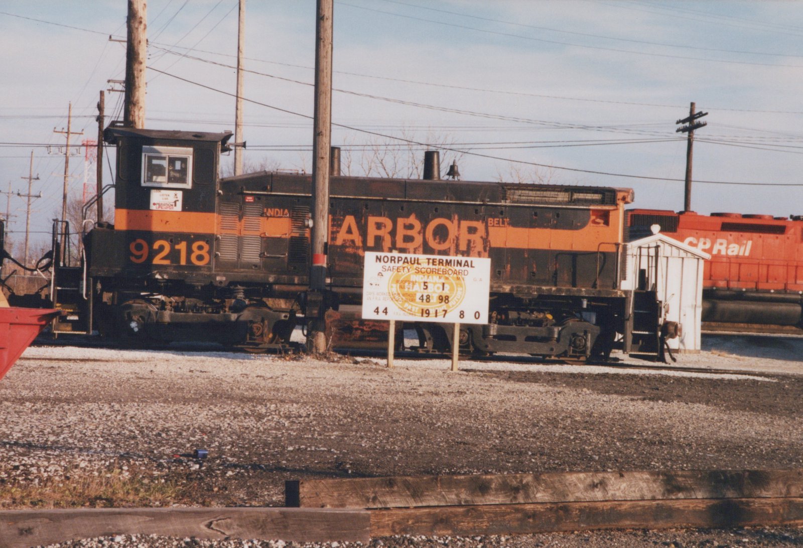 A weathered black and orange switcher locomotive numbered 9218 stands on a gravel-lined track behind a white safety sign, with a red CP Rail locomotive at the right.