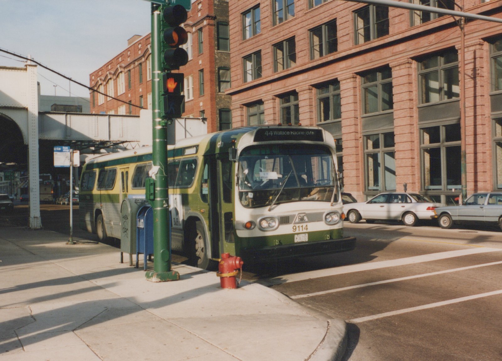 A green and cream CTA bus numbered 9114 is stopped at a street corner, with a destination sign reading 44 Wallace/Harline/67th and a white building in the background.