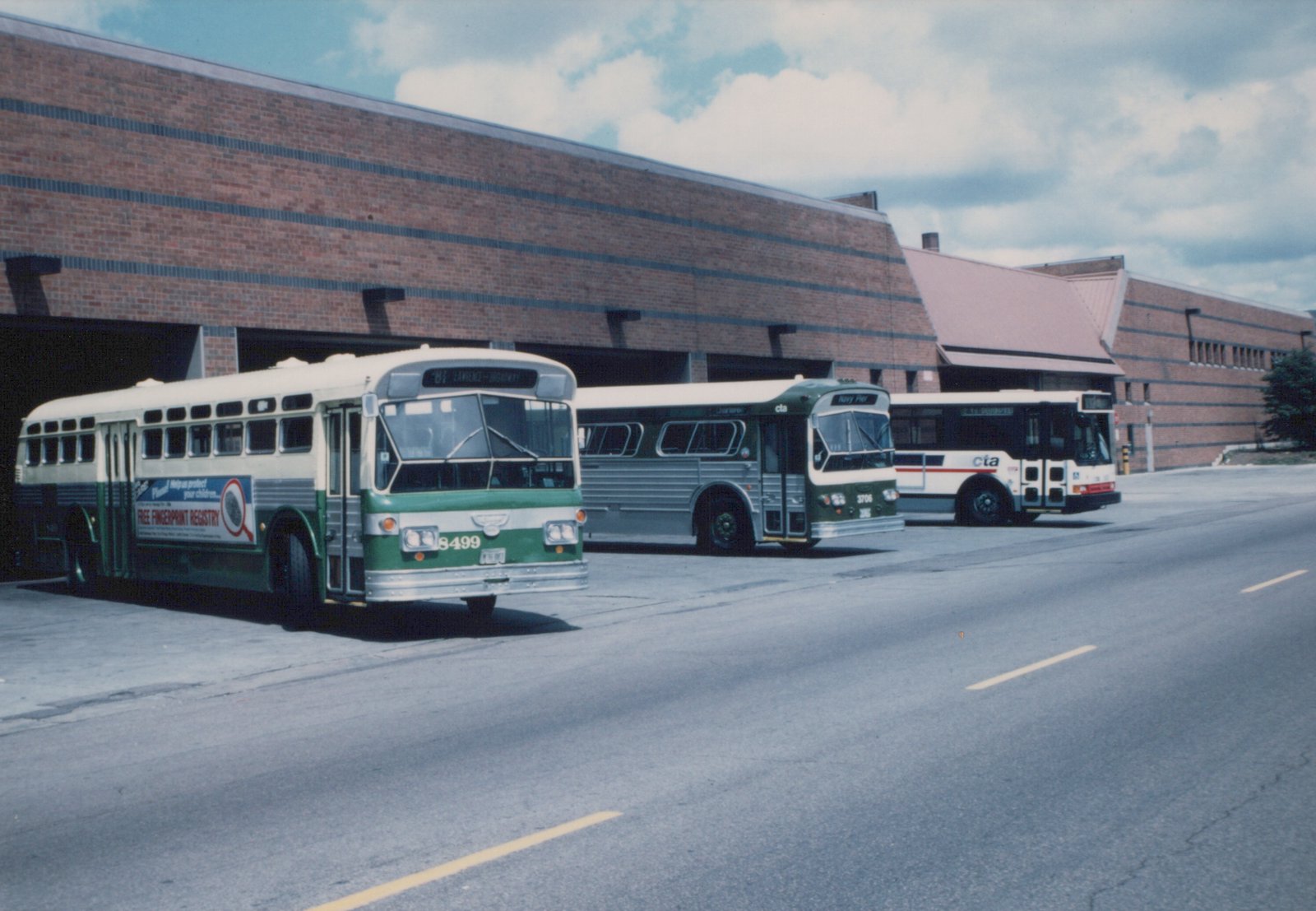 Three CTA buses, one green and two in white or dark green livery, parked in front of a brick building with garage doors.