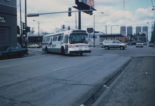 A white and red CTA bus, number 9206, is stopped at an intersection on a cloudy day, with cars and buildings in the background.