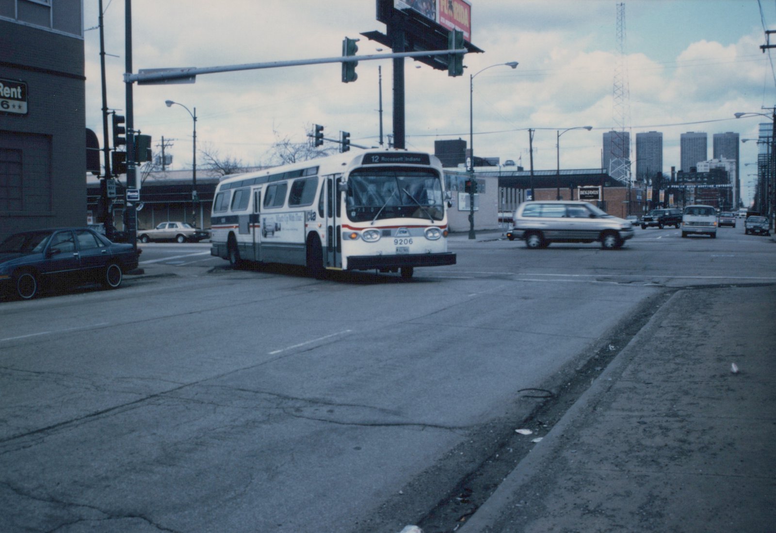 A white and red CTA bus, number 9206, is stopped at an intersection on a cloudy day, with cars and buildings in the background.