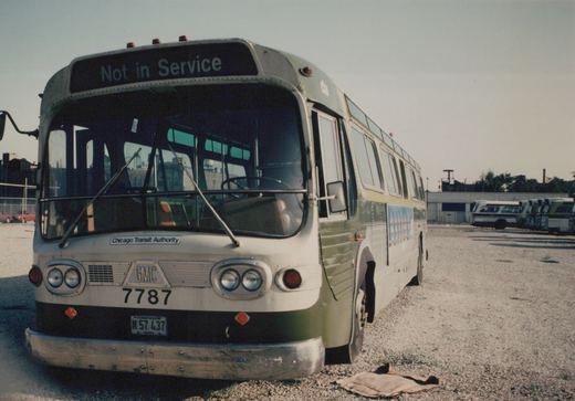 A three-quarter front view of a green and cream Chicago Transit Authority bus, number 7787, parked in a gravel lot with other buses in the background under a clear sky.