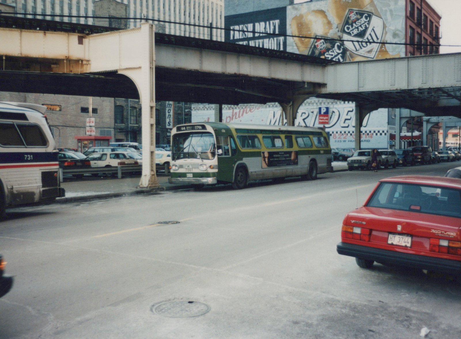 A green and white CTA bus, number 7861, is shown from the front, with another CTA bus, number 731, partially visible to the left. A red Volvo 740 Turbo is in the foreground. The scene is under a large, rusty elevated train structure on a snowy street.