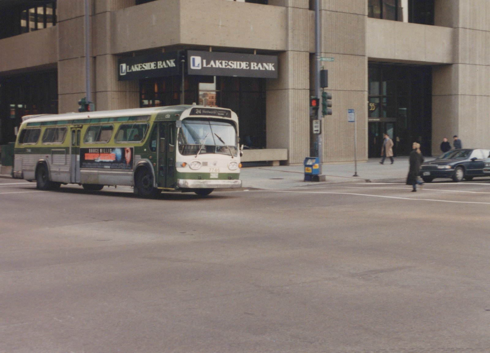 A green and cream CTA bus is stopped at an intersection in front of a building with a Lakeside Bank sign, with pedestrians crossing the street.