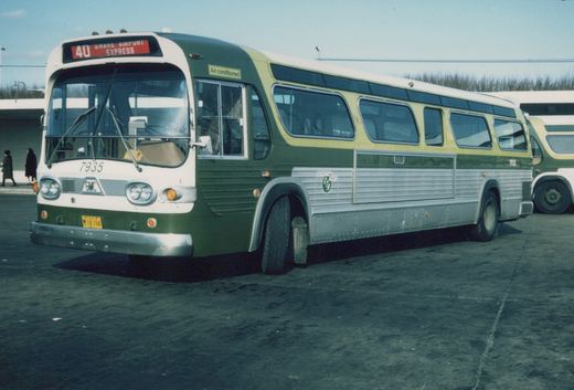 A green, white, and silver CTA bus numbered 7935, with a front sign reading '40 OHARE AIRPORT EXPRESS', parked outdoors in winter with two people walking in the background.