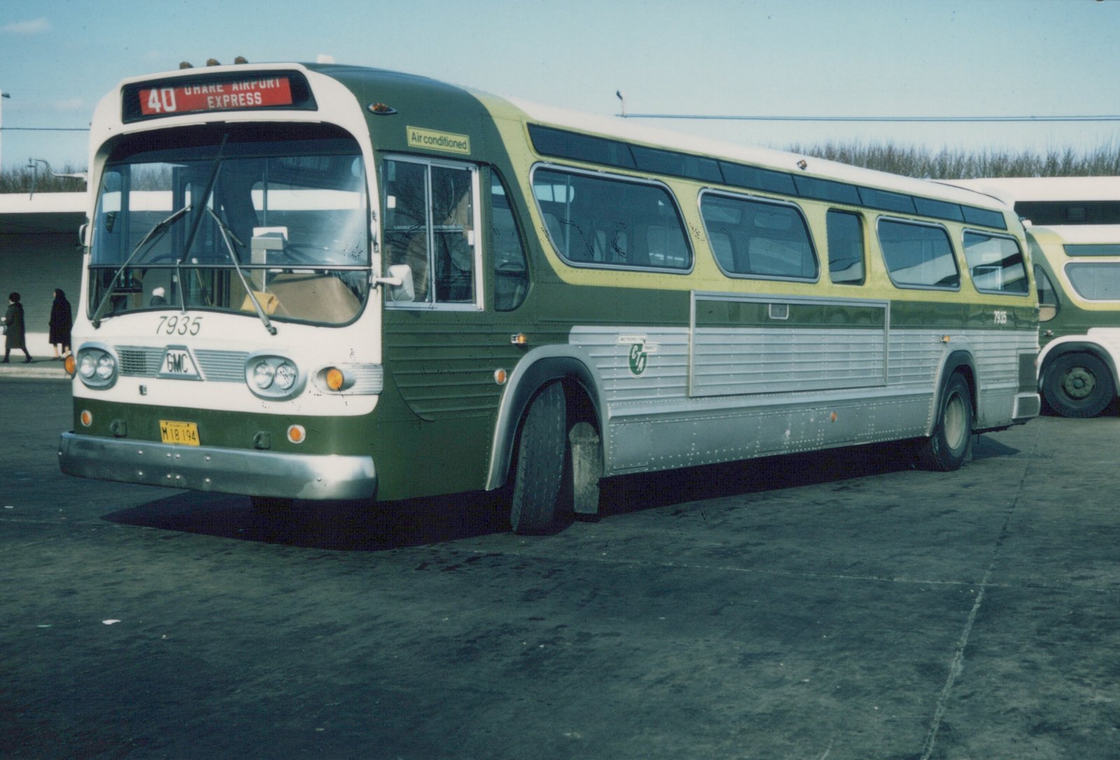 A green, white, and silver CTA bus numbered 7935, with a front sign reading '40 OHARE AIRPORT EXPRESS', parked outdoors in winter with two people walking in the background.