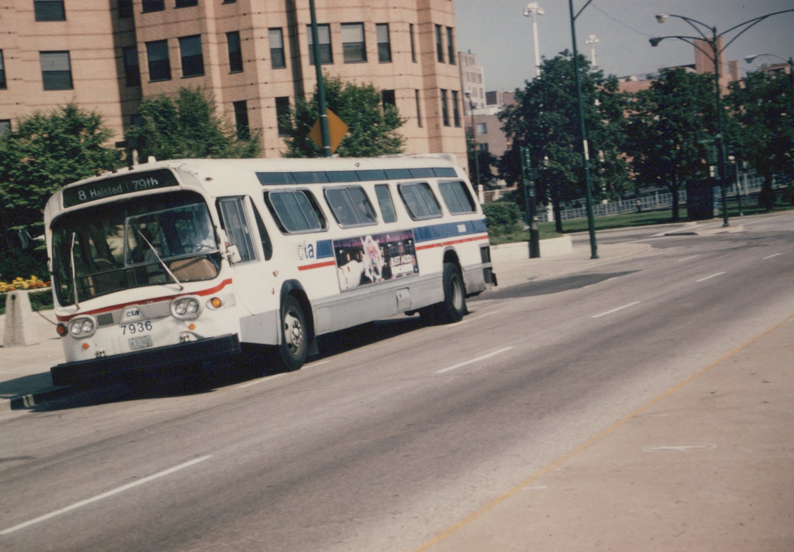 A white Chicago Transit Authority bus with blue and red stripes, numbered 7936, drives down a city street on a clear day.