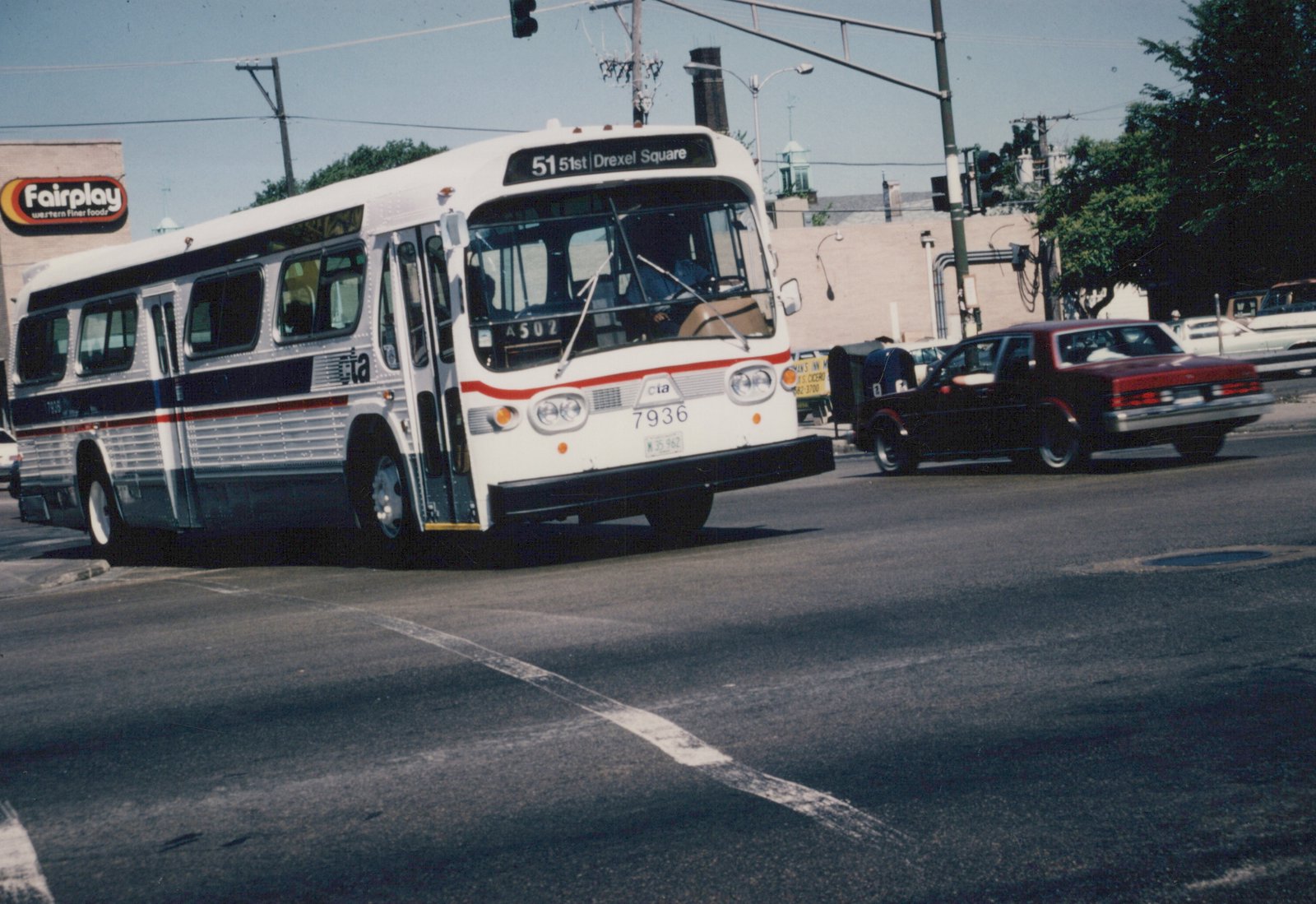 A white and blue CTA bus with the number 7936 is turning onto a city street, with a red car and a Fairplay store sign visible in the background.