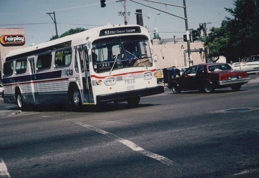 A white and blue CTA bus with the number 7936 is turning onto a city street, with a red car and a Fairplay store sign visible in the background.