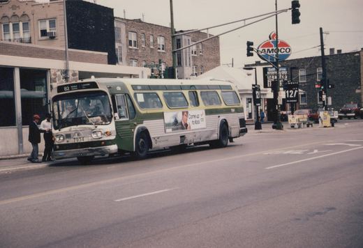 A green and cream Chicago Transit Authority bus numbered 7934, with route 82 to Kimball Homan, is stopped on a street next to pedestrians and buildings, with an Amoco sign in the background.