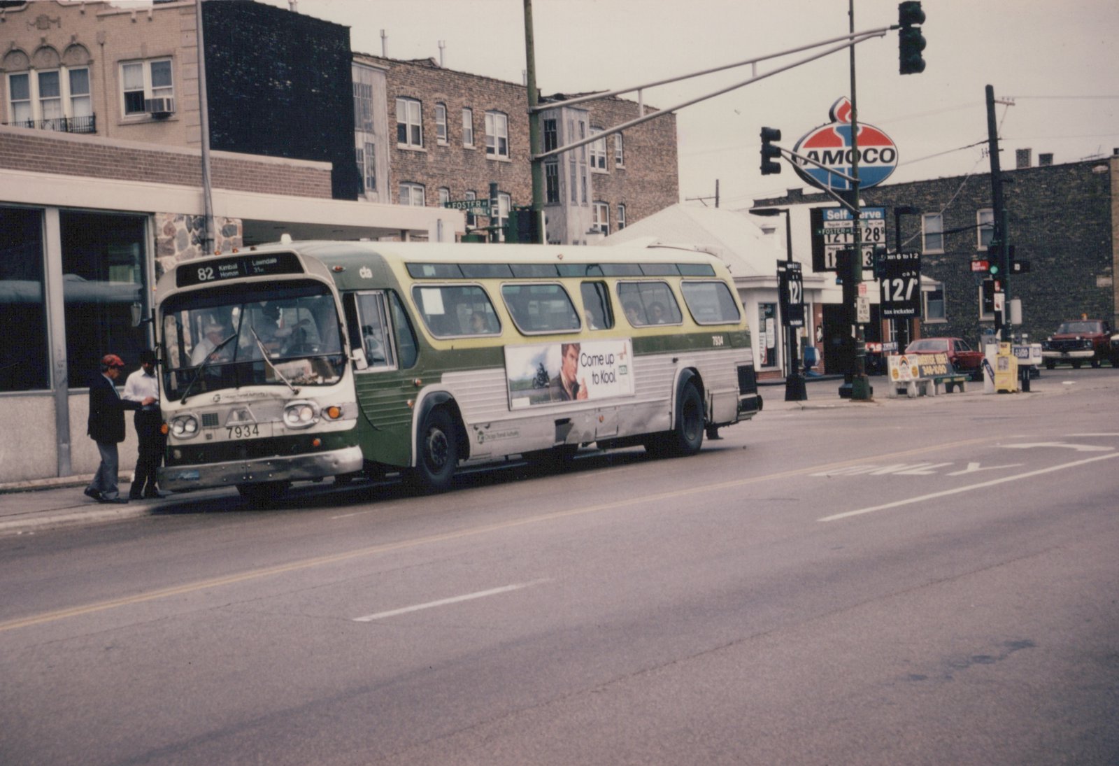 A green and cream Chicago Transit Authority bus numbered 7934, with route 82 to Kimball Homan, is stopped on a street next to pedestrians and buildings, with an Amoco sign in the background.