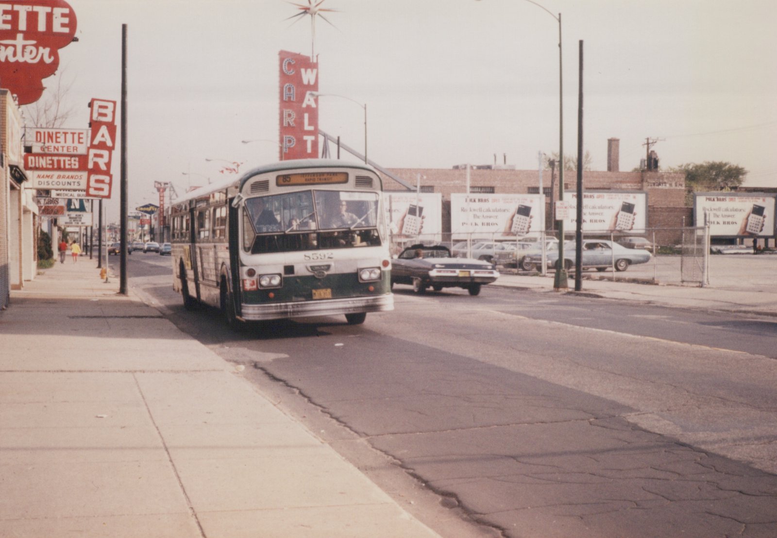 A green and white motor bus with the number 5592 travels on a city street, with pedestrians on the sidewalk and vintage signs for 'DINETTE CENTER' and 'CARLPT' visible in the background.