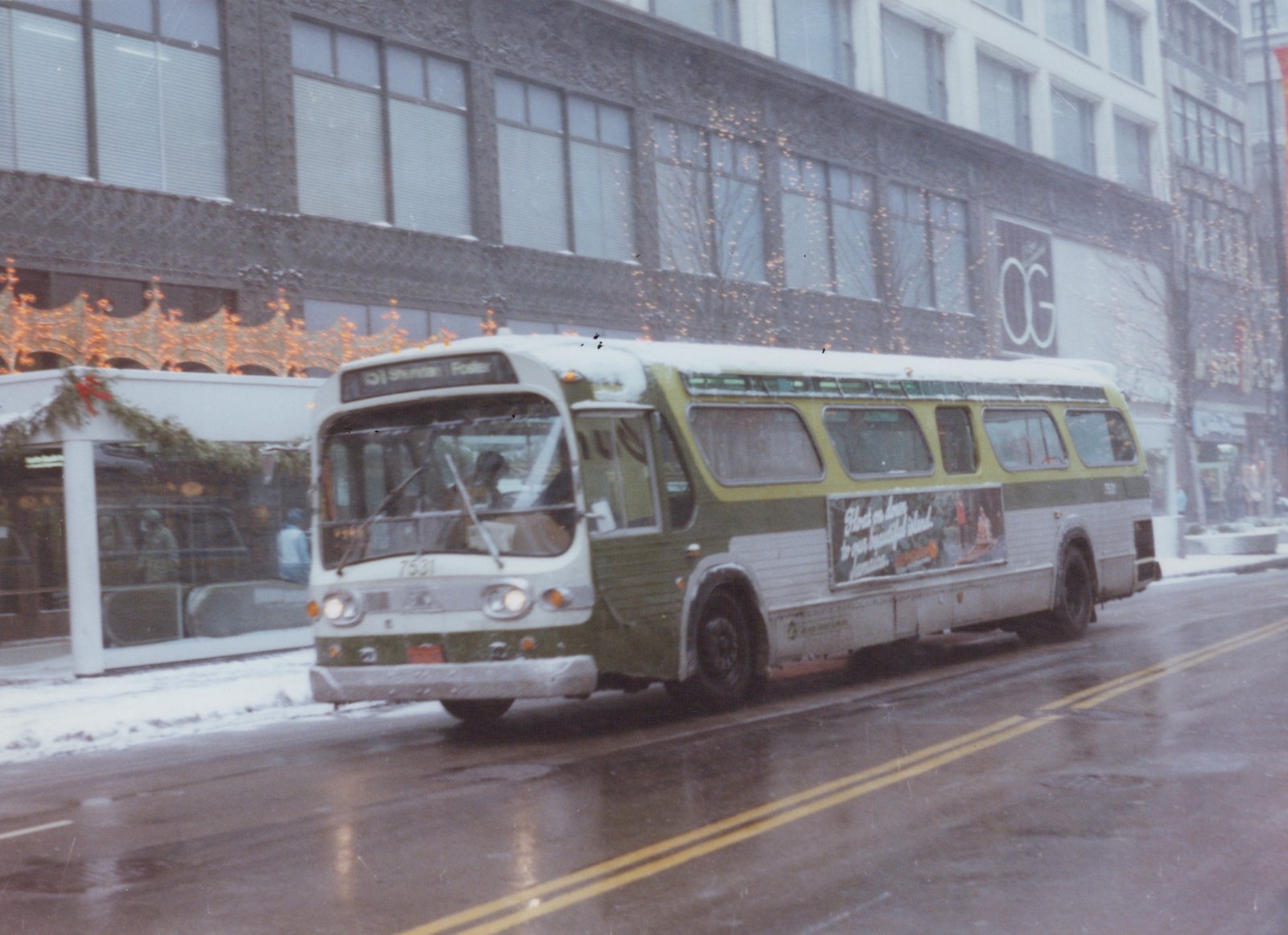 A green and white CTA bus with the route sign reading '51 Sheridan / Foster' drives on a wet, snow-covered street with Christmas decorations visible on a storefront in the background.