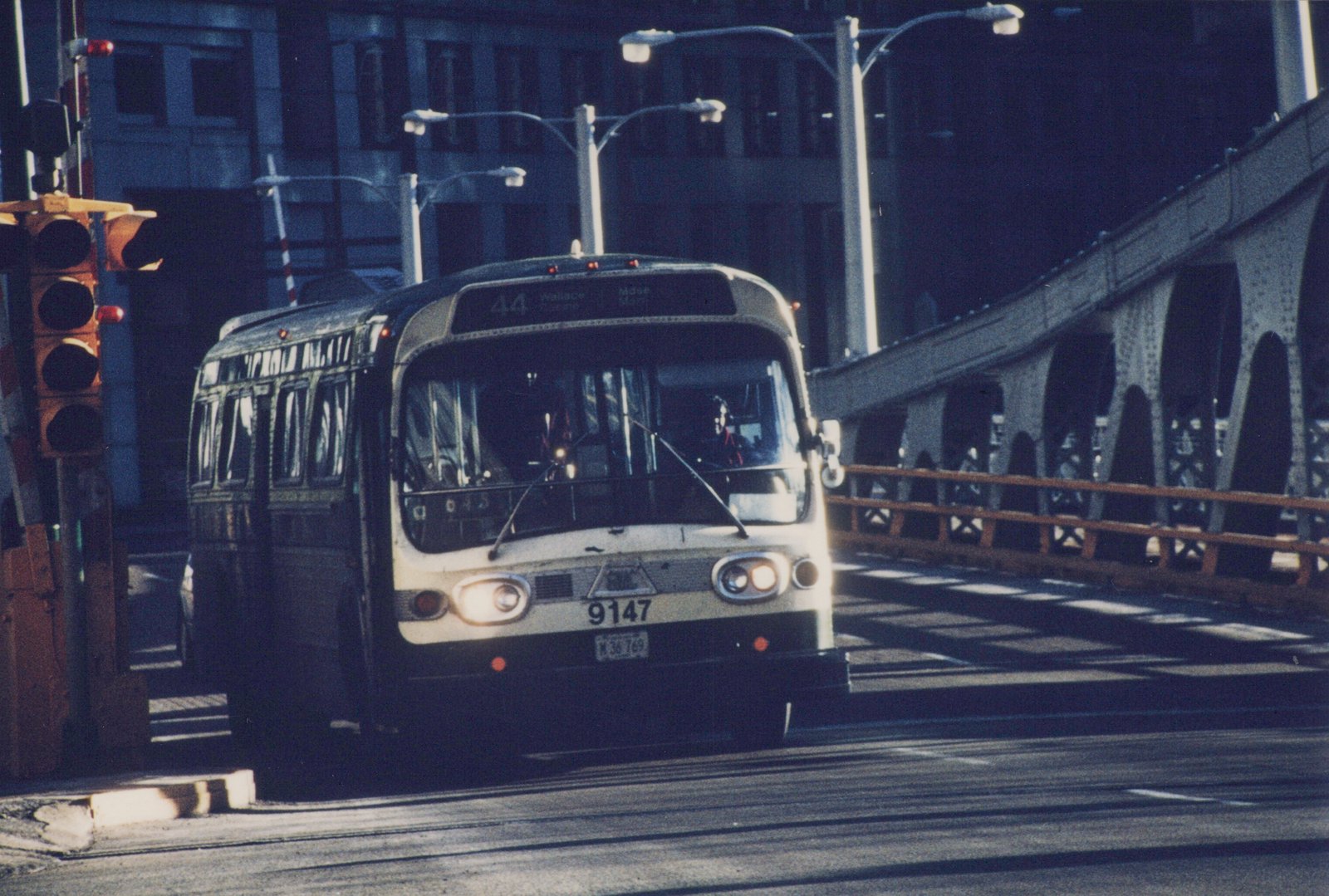 A white and black Chicago Transit Authority bus, number 9147, drives across a steel bridge in daylight with a traffic light visible on the left.