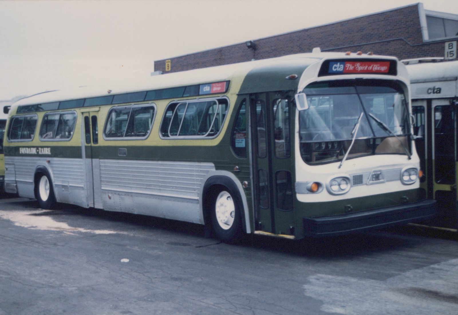 A green, cream, and silver CTA bus with the number P9999 on its windshield is parked in a bus garage on an overcast winter day.