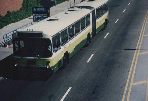 An elevated view of a green, yellow, and white Chicago Transit Authority articulated bus, number 7178, driving on a multi-lane street with a sidewalk and business signs visible nearby.