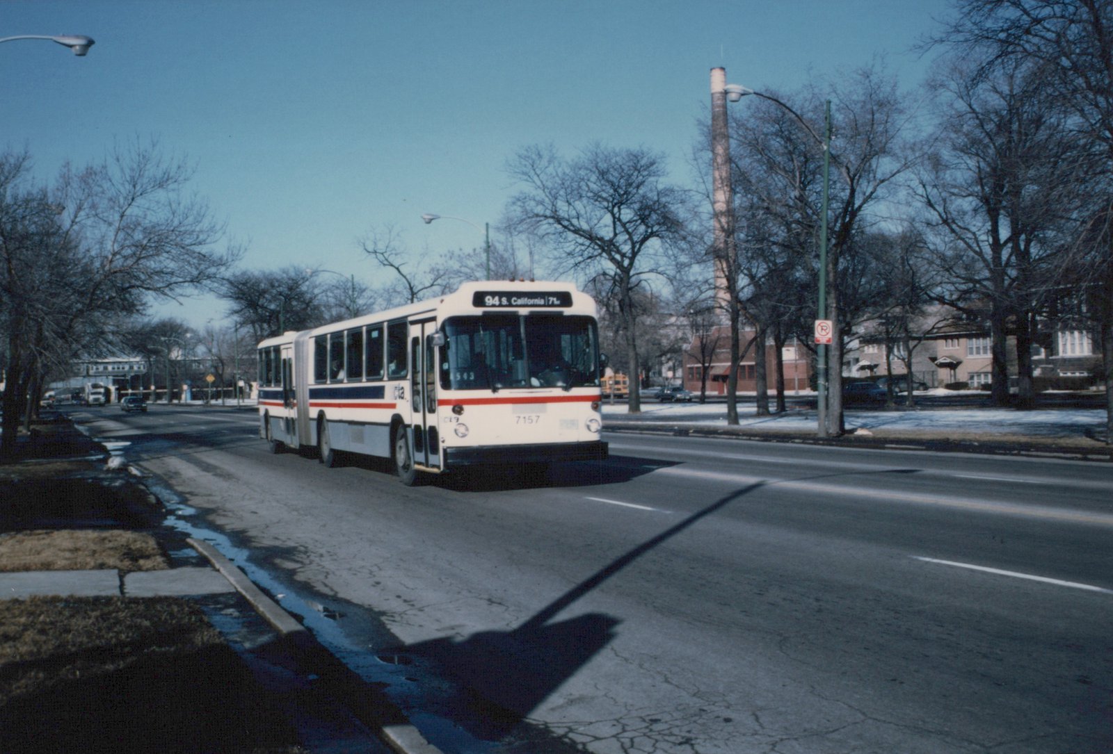An articulated CTA bus drives on a city street on a clear winter day, with bare trees and patches of snow visible.