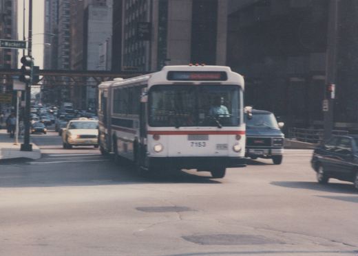 A white and red CTA bus, number 7153, is driving on a city street with other cars and an elevated structure in the background.