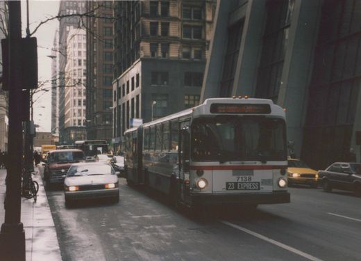 A white and red CTA bus marked 7138 on the 23 Express route is driving down a wet city street lined with tall buildings, with other cars and a taxi nearby.