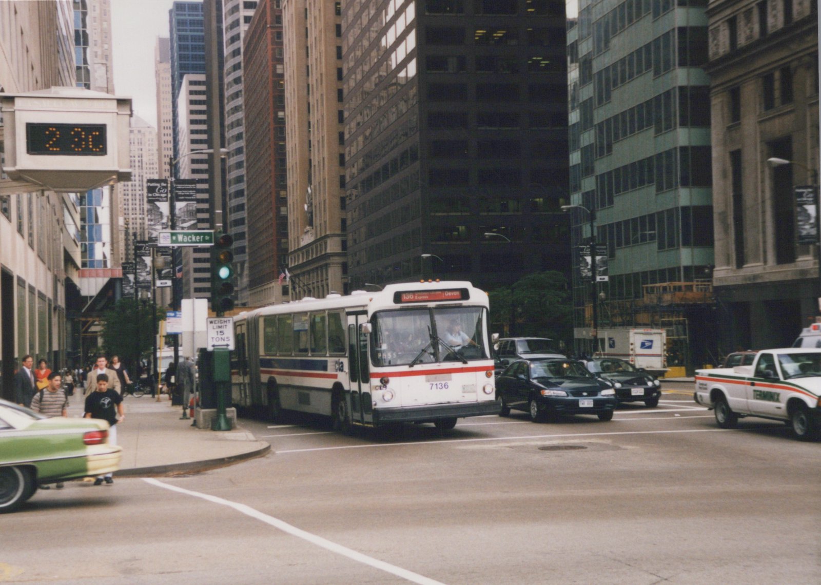 A white CTA bus with the number 7136 and destination sign reading '136 Express Devon' is turning on a city street lined with tall buildings, with pedestrians on the sidewalk and other cars nearby.