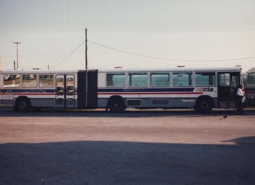 Side view of a white, blue, and red articulated bus with 'CTA' lettering and the number 7131, parked on a paved lot with a person standing nearby.