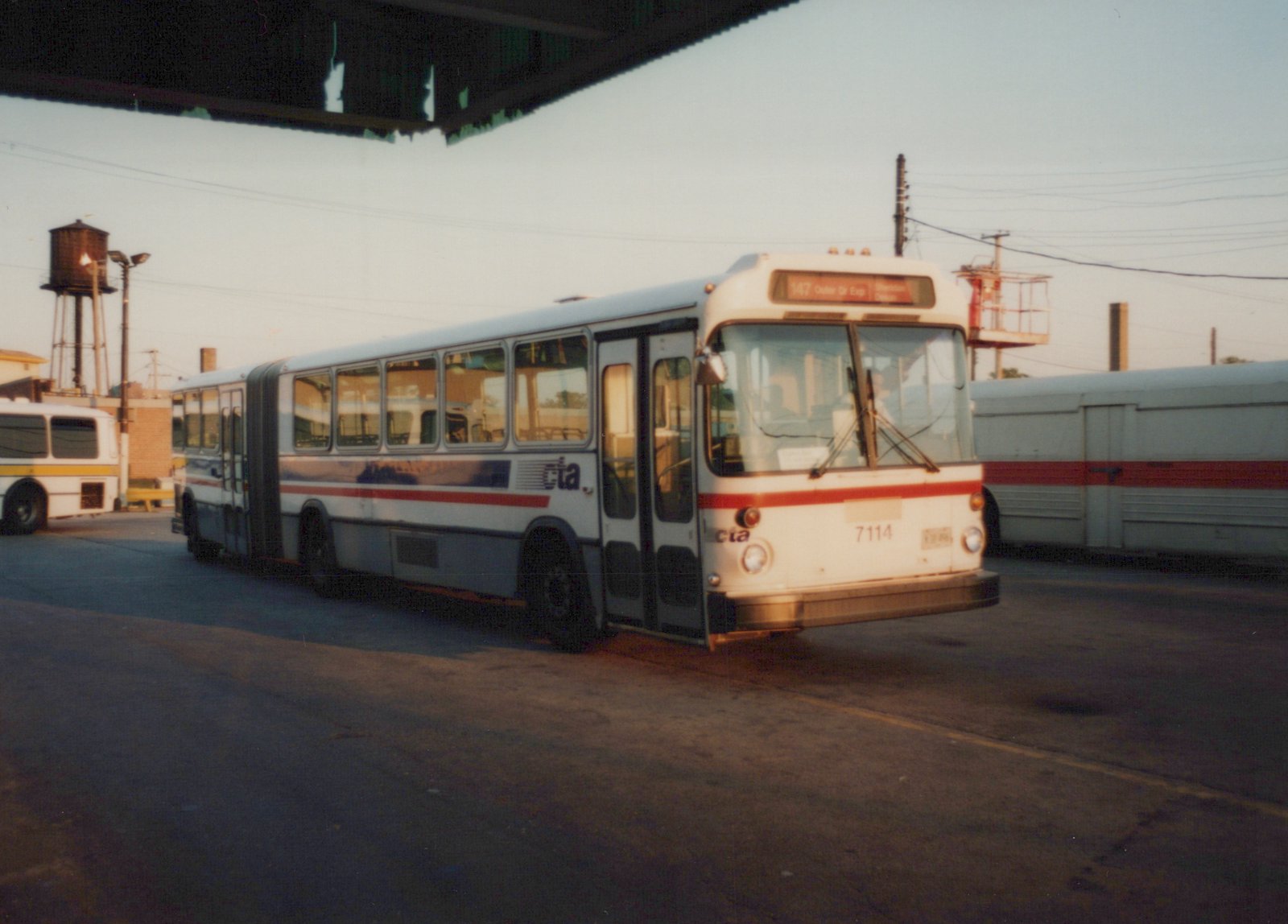 A white and red Chicago Transit Authority articulated bus, number 7114, with route 147 displayed, parked inside a bus garage with another bus visible in the background.
