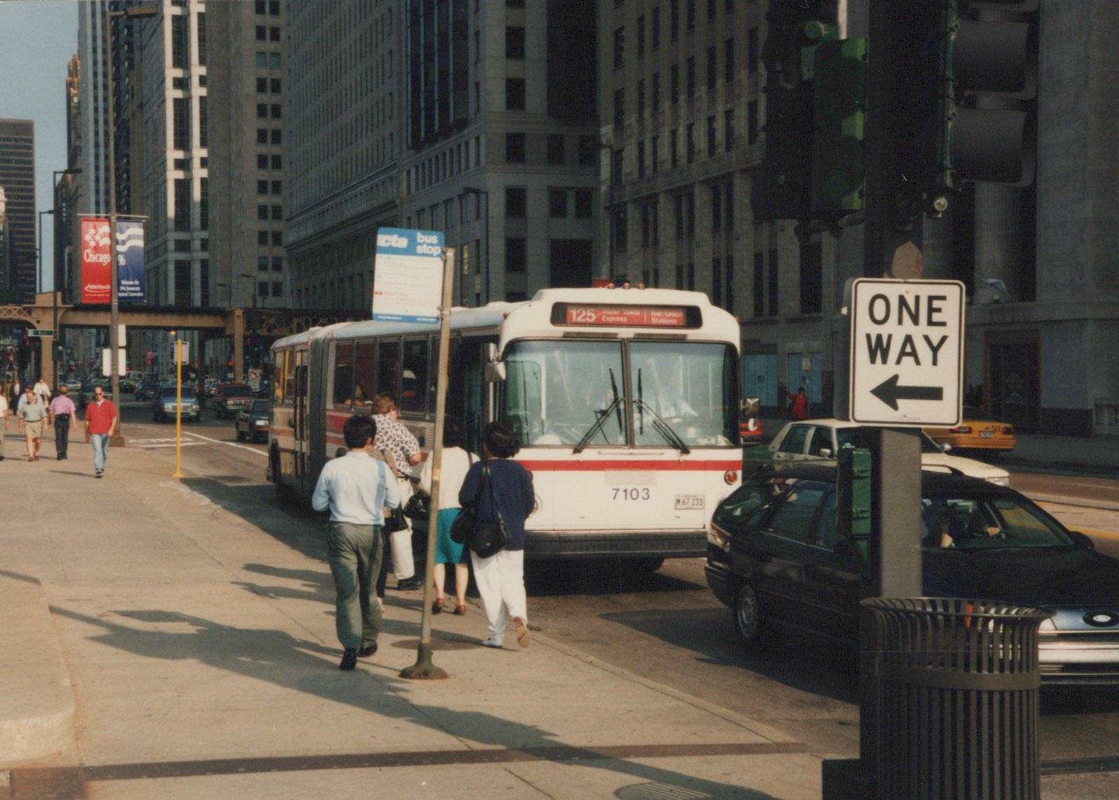 A white and red CTA bus numbered 7103 is stopped on a city street with passengers boarding. A 'Chicago '96' banner hangs from a pole, and a 'ONE WAY' sign is visible.