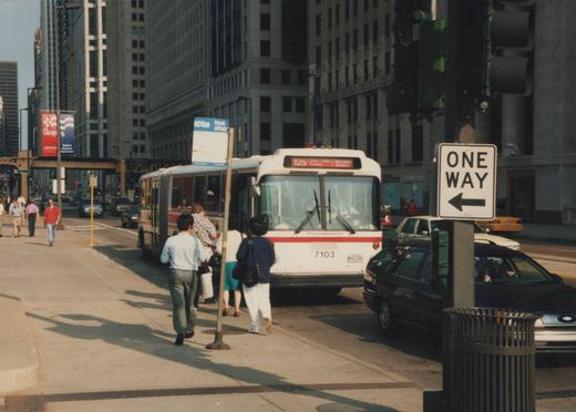 A white and red CTA bus numbered 7103 is stopped on a city street with passengers boarding. A 'Chicago '96' banner hangs from a pole, and a 'ONE WAY' sign is visible.