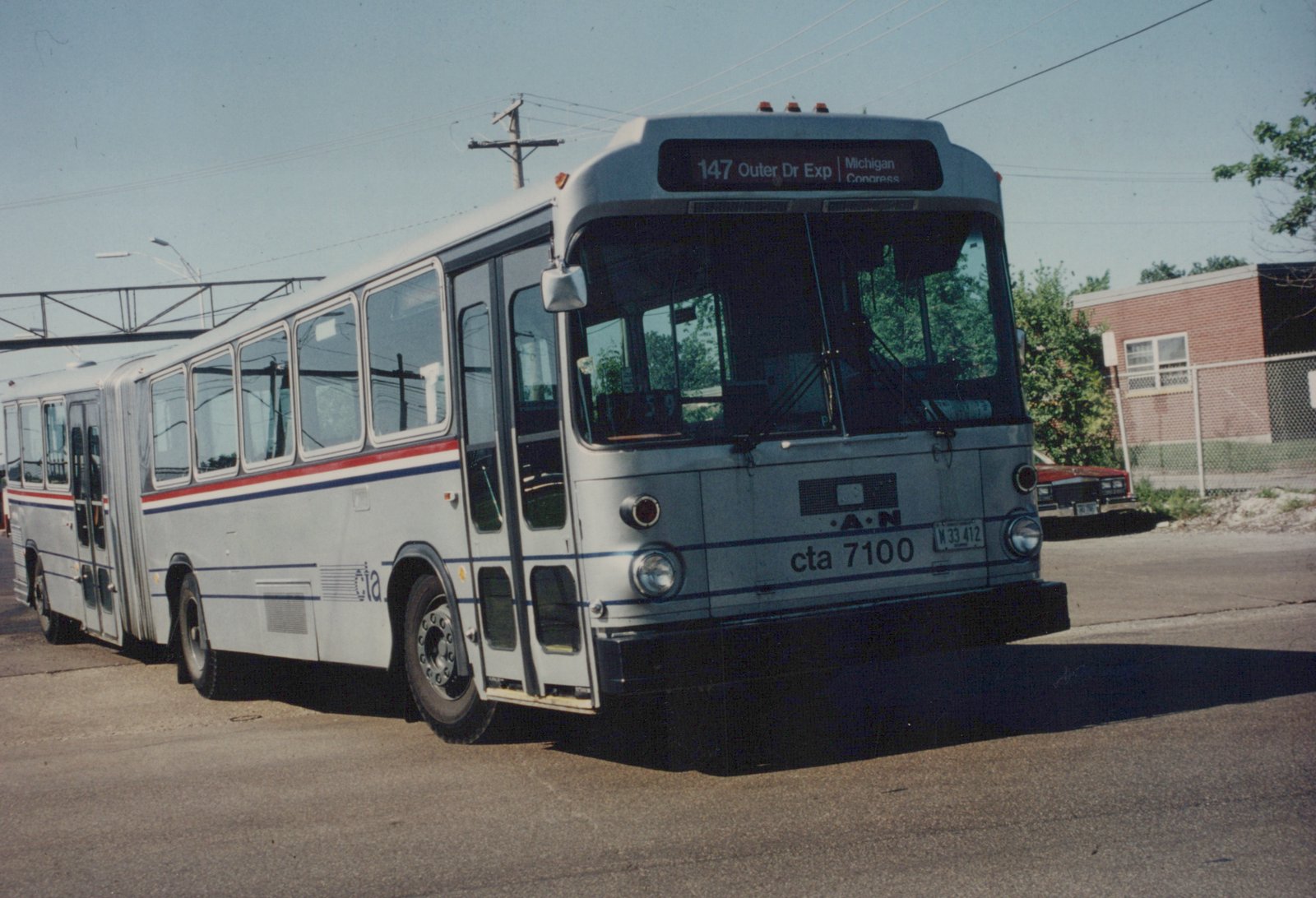 CTA articulated bus number 7100 on a clear day, displaying route 147 Outer Dr Exp, parked on a street near a brick building.