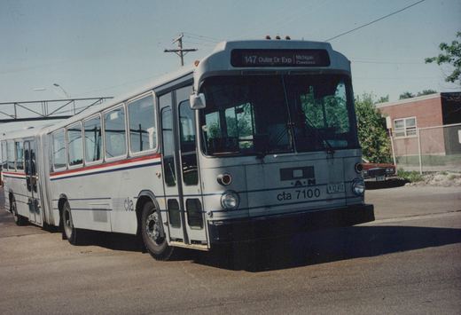 CTA articulated bus number 7100 on a clear day, displaying route 147 Outer Dr Exp, parked on a street near a brick building.