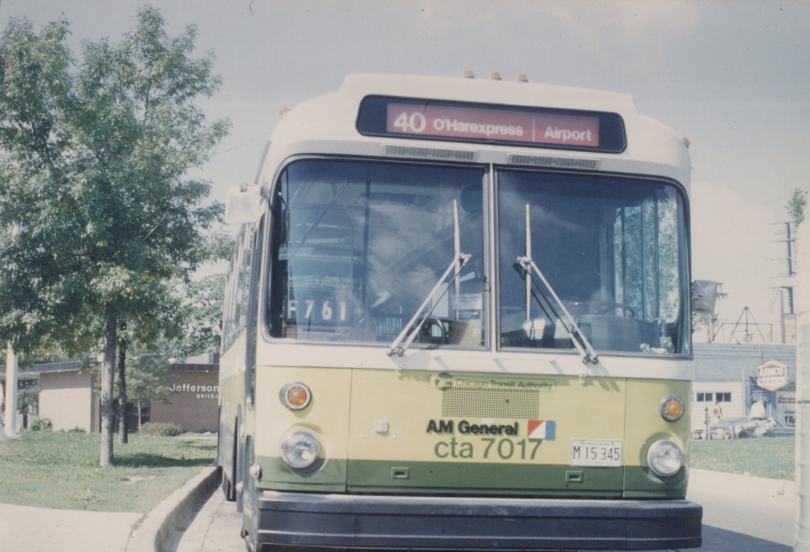 Front view of a green and cream Chicago Transit Authority bus with the destination '40 O'Harexpress | Airport' displayed, parked on a street with trees and a building in the background.