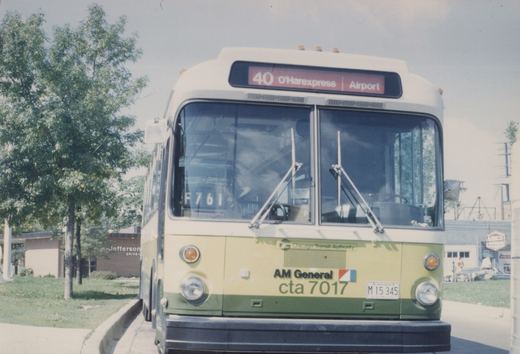 Front view of a green and cream Chicago Transit Authority bus with the destination '40 O'Harexpress | Airport' displayed, parked on a street with trees and a building in the background.