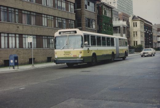 A yellow, green and cream articulated bus from the Chicago Transit Authority, numbered 7011, is on a city street. A street sign in the background reads 'Clarendon + Lawrence'.