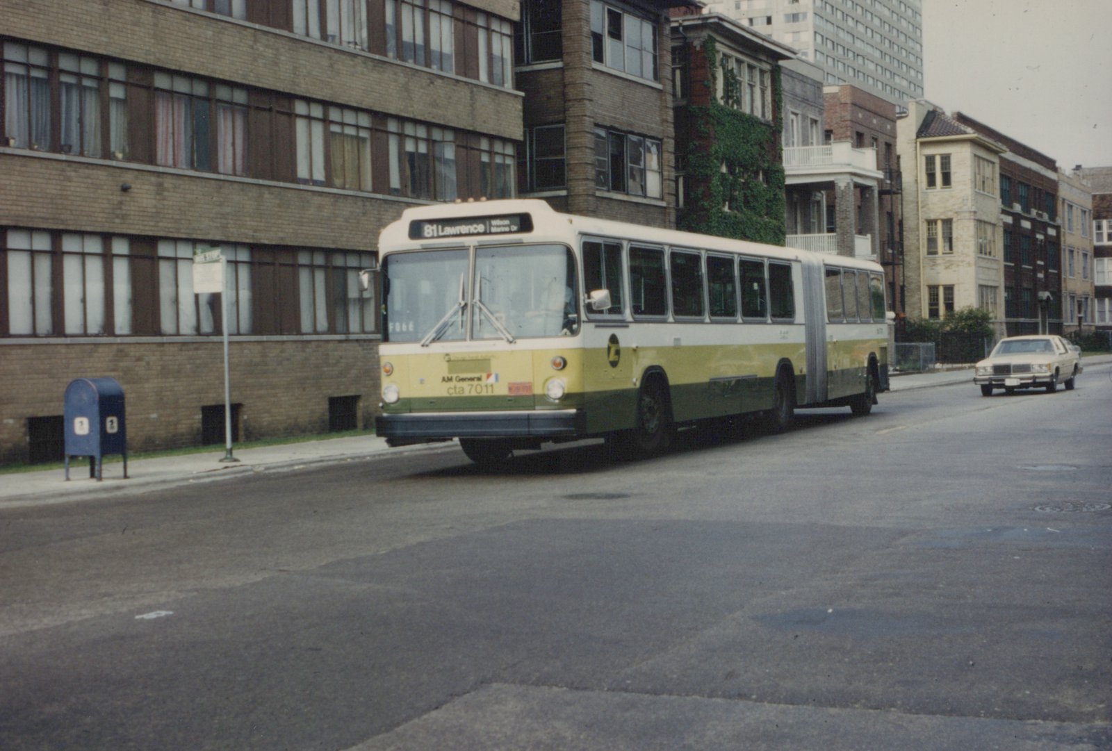 A yellow, green and cream articulated bus from the Chicago Transit Authority, numbered 7011, is on a city street. A street sign in the background reads 'Clarendon + Lawrence'.