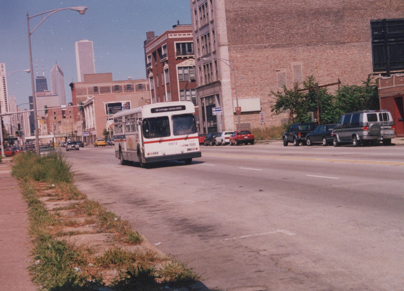A white and red CTA bus, number 9972, drives down a city street on a clear day with tall buildings in the distance.