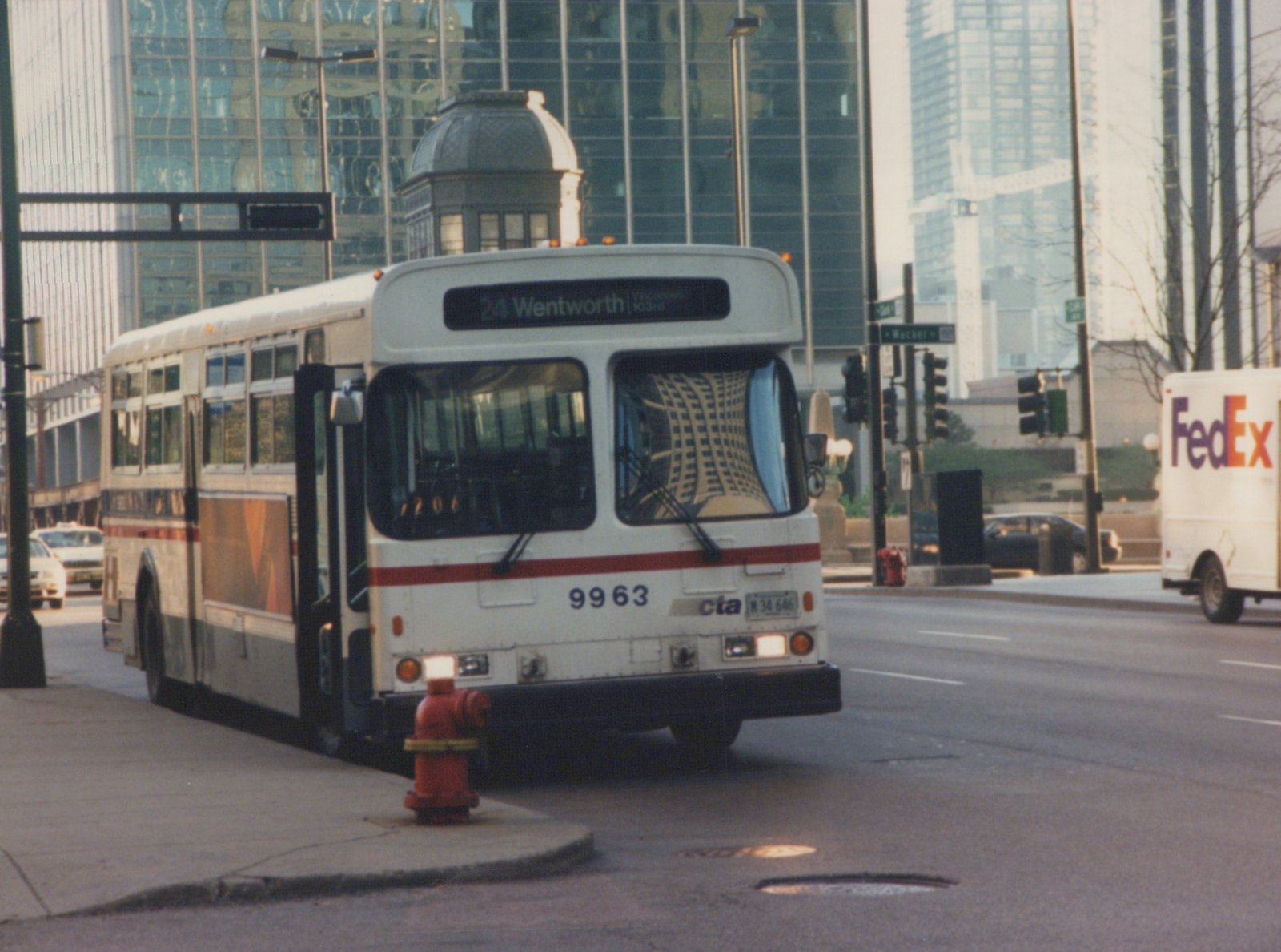 A white and red CTA bus with the number 9963 is driving on a city street with tall buildings in the background.