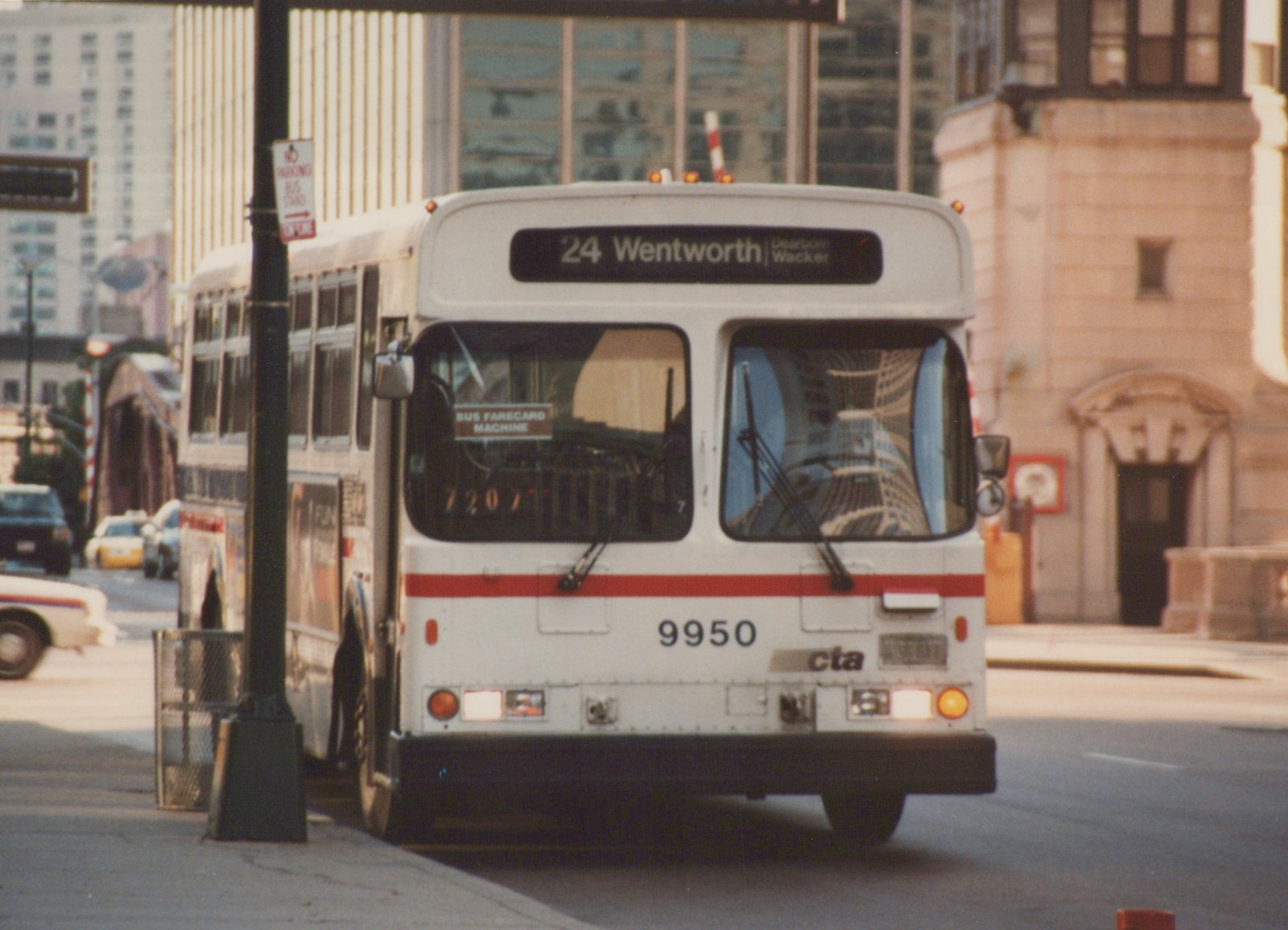Front view of a white and red CTA bus numbered 9950 on route 24 Wentworth, parked on a city street with buildings and other cars in the background.