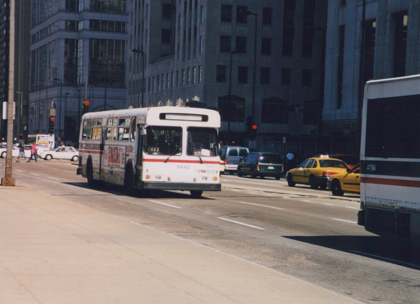 A white and red CTA bus, number 9940, is driving on a multi-lane city street with tall buildings in the background and other vehicles nearby.