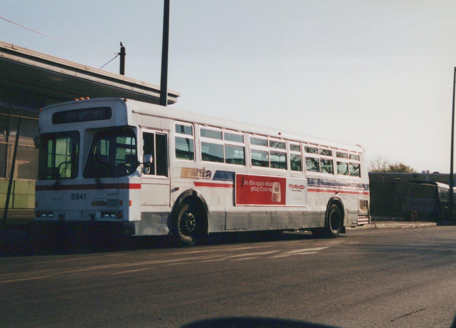 A side view of a white Chicago Transit Authority bus with the number 9941 on the front and rear, parked on a street with a clear sky and another bus visible in the background.