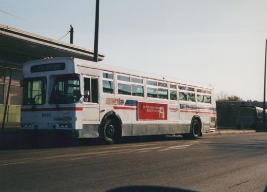 A side view of a white Chicago Transit Authority bus with the number 9941 on the front and rear, parked on a street with a clear sky and another bus visible in the background.