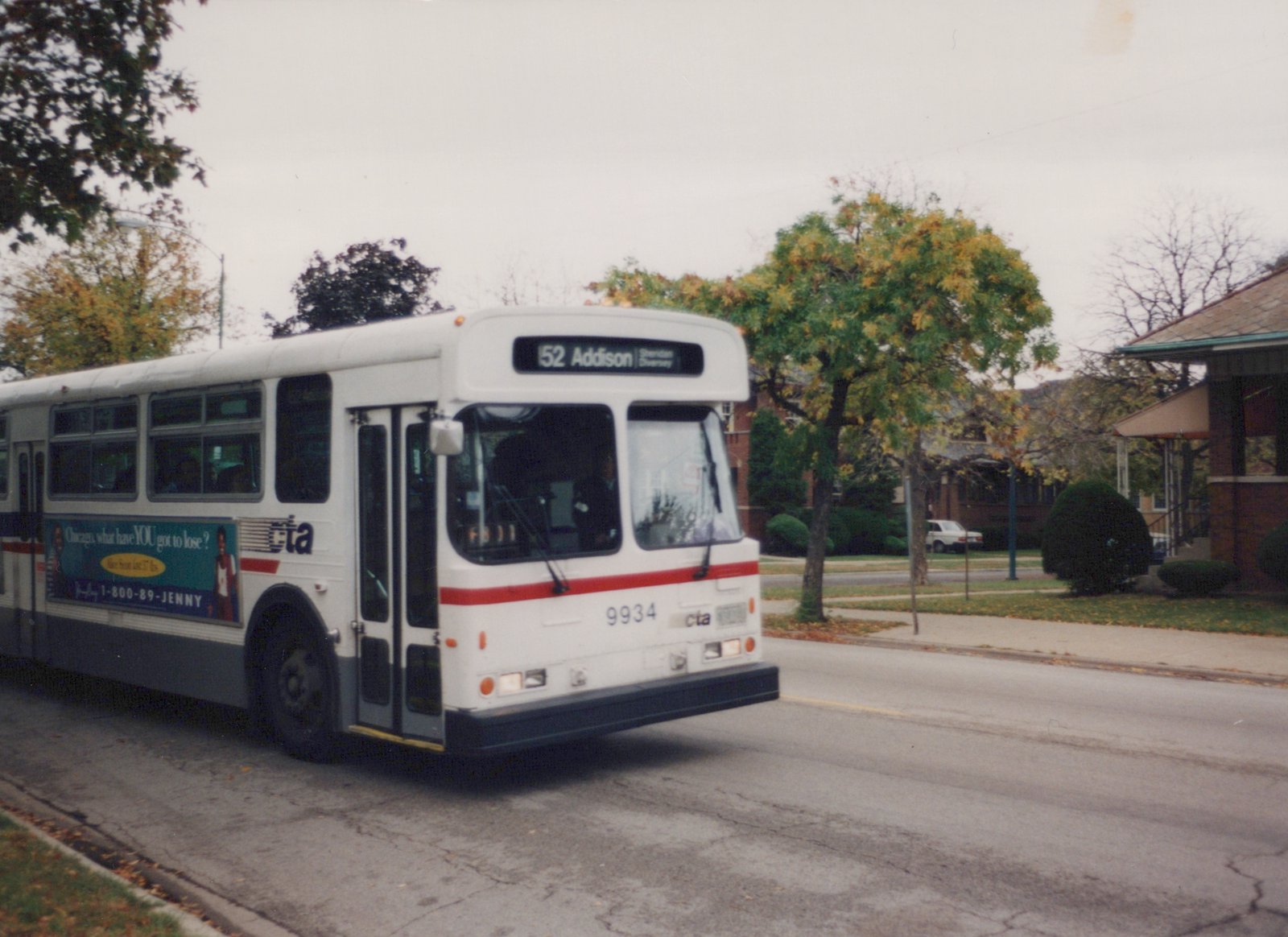 A white CTA bus numbered 9934, running on Route 52 Addison, is shown from a three-quarter front view on a residential street with autumn leaves.