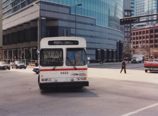 Front view of a white CTA bus with red stripe, number 9922, on a city street with tall buildings and other vehicles in the background.