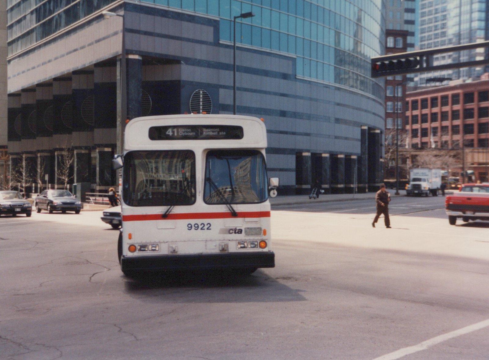 Front view of a white CTA bus with red stripe, number 9922, on a city street with tall buildings and other vehicles in the background.