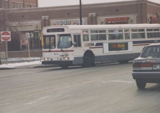 A white CTA bus with fleet number 9916 and route 64 Austin on its sign is turning on a snowy street corner, with a Dunkin' Donuts and Baskin-Robbins visible behind it.