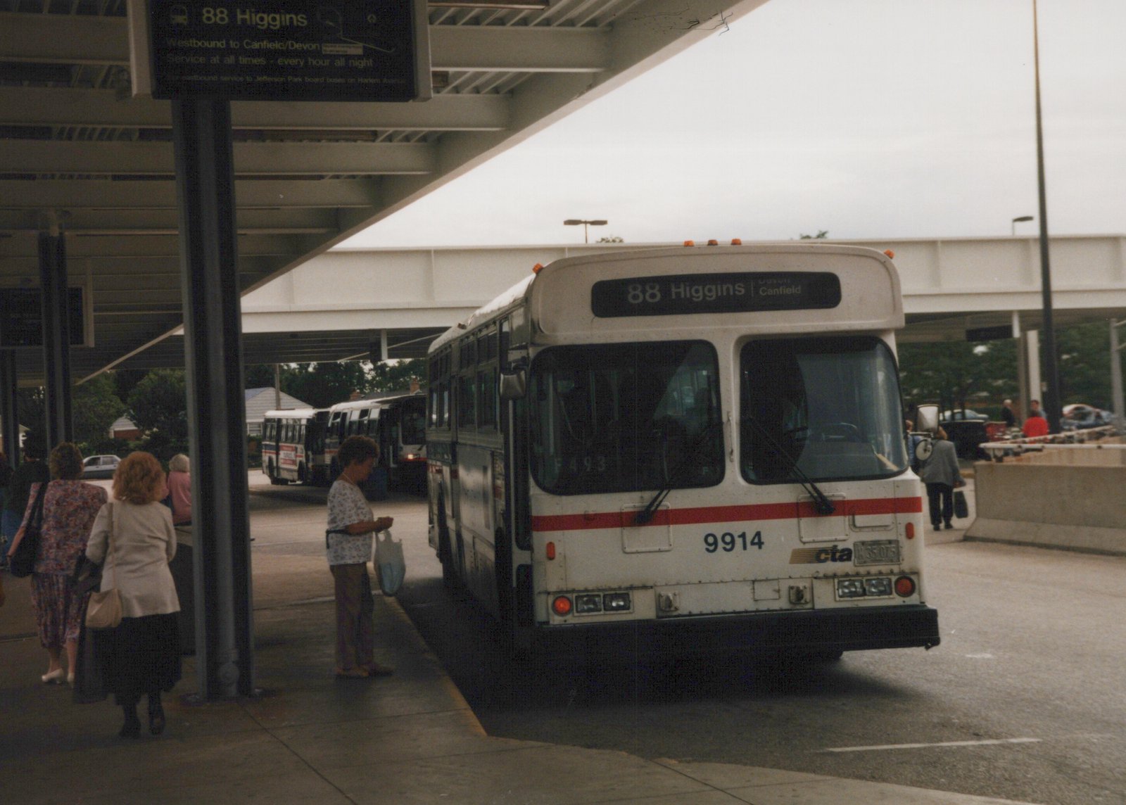 A white CTA bus with the number 9914 and route 88 Higgins displayed is parked at a covered terminal with several people nearby.