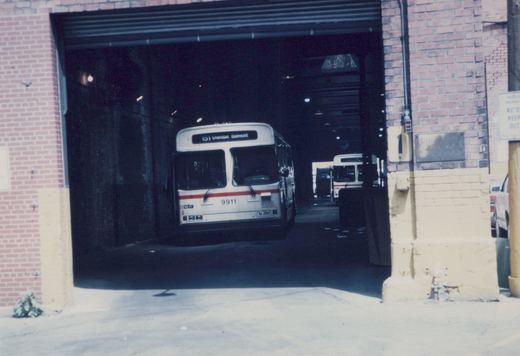 Front view of a white and red CTA bus, fleet number 9911, parked in a brick garage with snow on the ground outside.