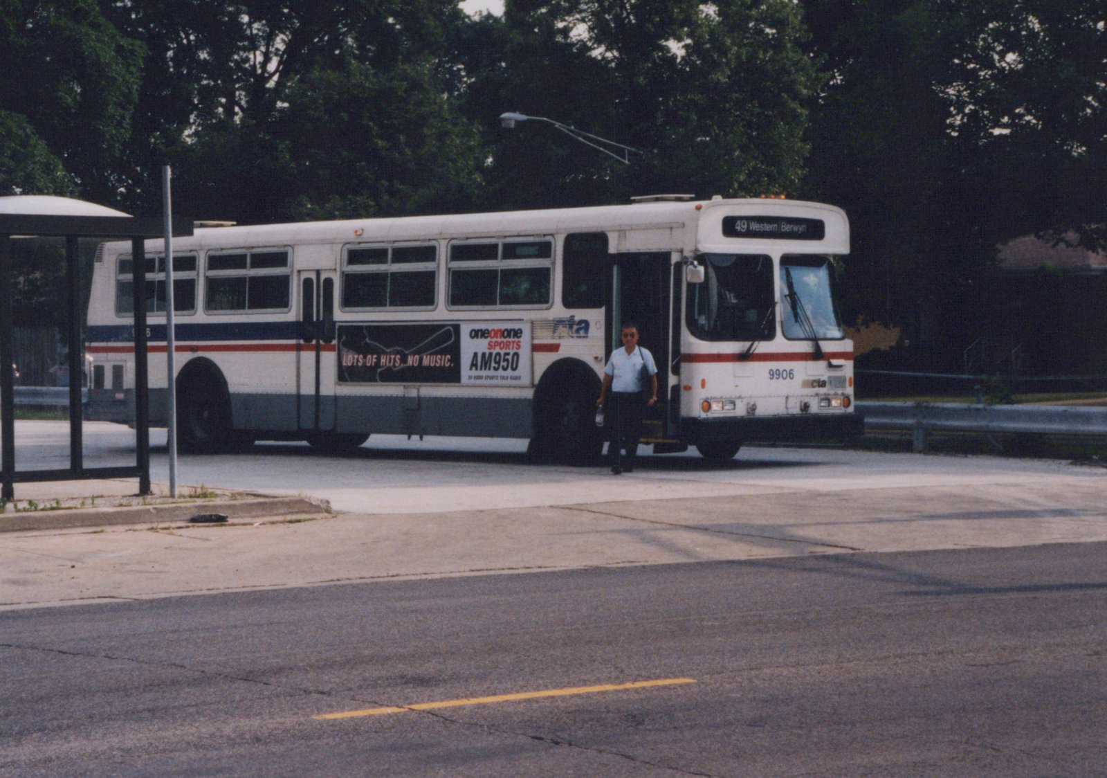 A white CTA bus with a blue and red stripe, number 9906, parked on a street with a driver standing at the doorway; the destination sign reads '49 Western Berwyn'.