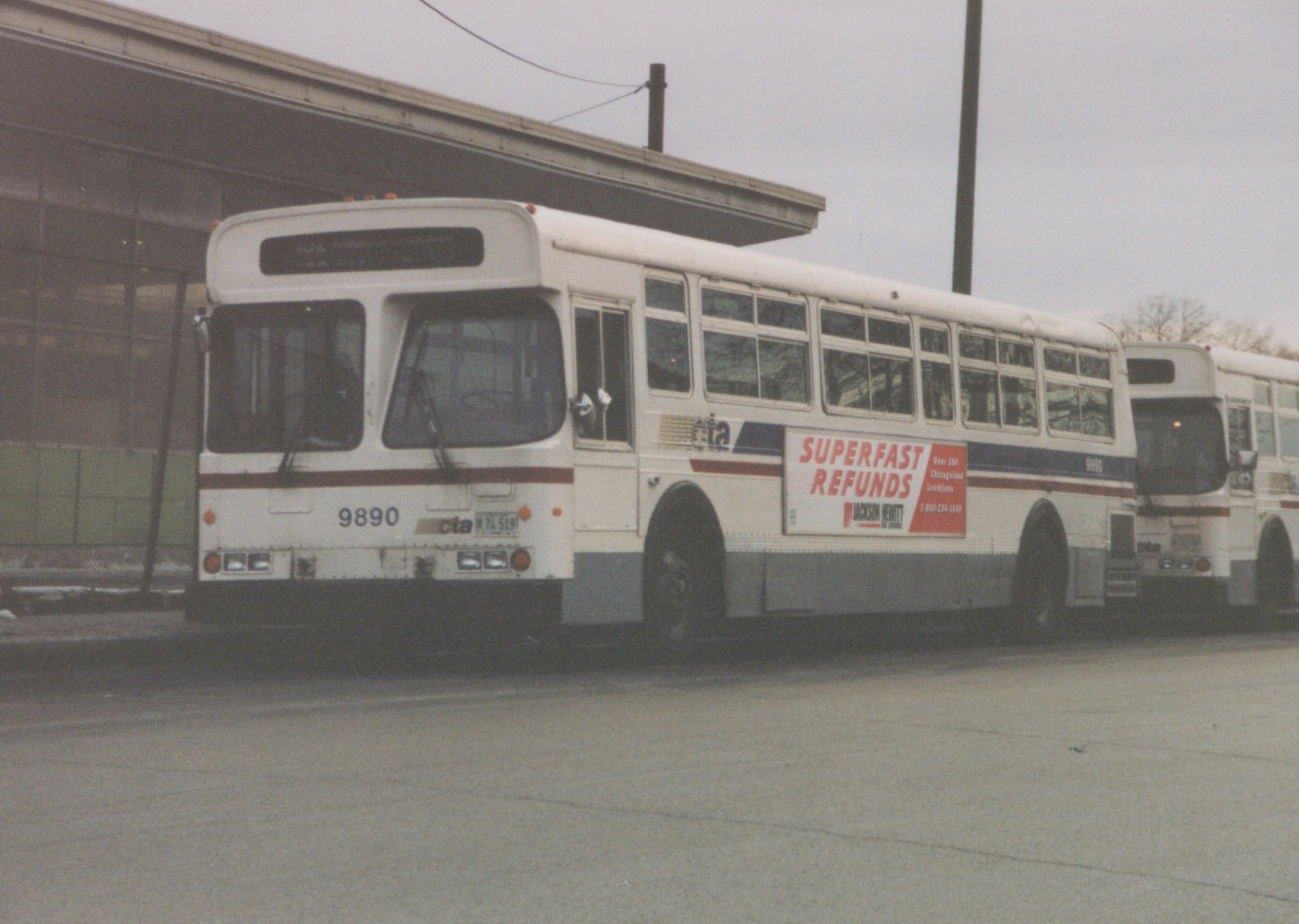 A white Chicago Transit Authority bus with the number 9890, featuring a Jackson Hewitt advertisement, parked outside a building.