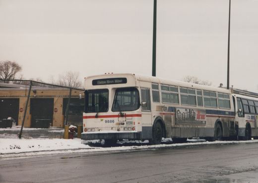 A white Chicago Transit Authority bus with red and blue stripes, number 9886, parked in front of a garage with snow on the ground and an ad for 'The Sopranos' on its side.